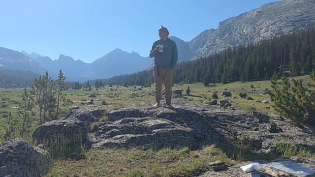 A hiker standing on a granite slab with mountains behind