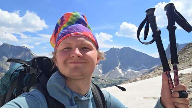 Finn in a tie-dye bandana holding up trekking poles below the peaks