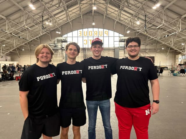 Four teammates in matching robotics shirts in a big arena