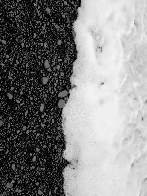 Black-and-white photo of surf foam meeting black sand