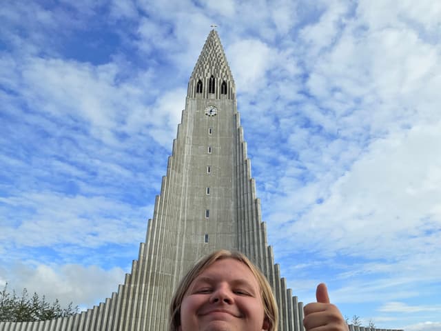 Finn grinning in front of the tall concrete spire of Hallgrímskirkja church