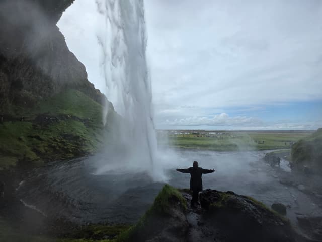A person with arms spread on a rock beside the falling water of Seljalandsfoss