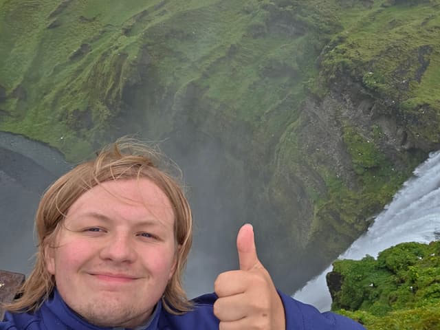 Finn smiling with a thumbs up beside Skógafoss