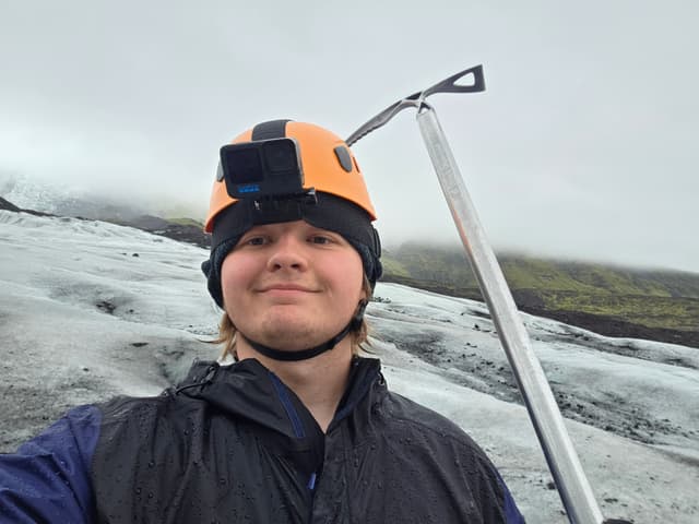 Finn in a helmet holding an ice axe on the glacier