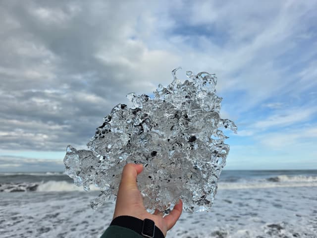 A hand holding up a clear chunk of glacier ice
