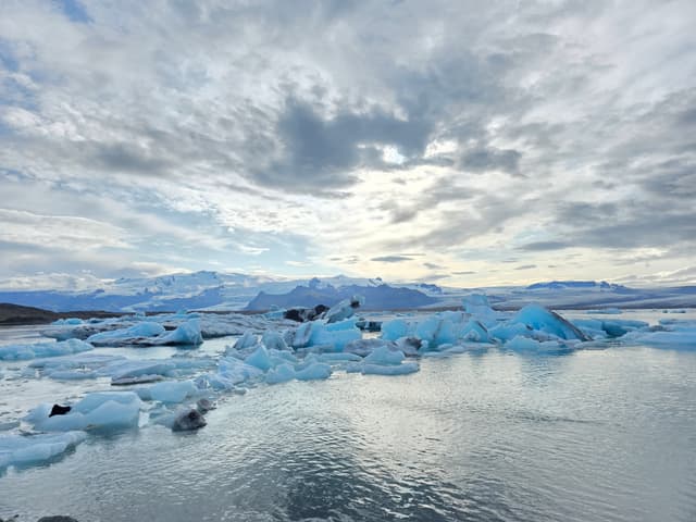 Blue icebergs floating in Jökulsárlón under a bright cloudy sky