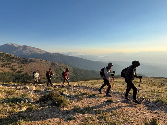 Hikers with trekking poles on an alpine ridge at sunrise
