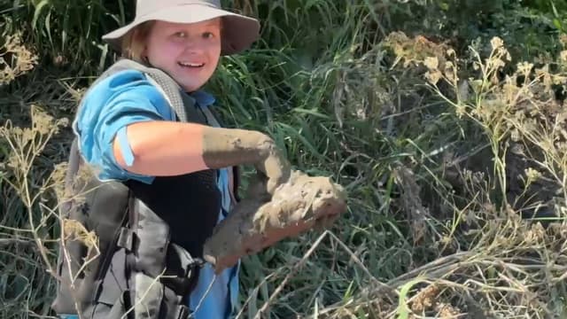 Finn in a life jacket holding a handful of river mud