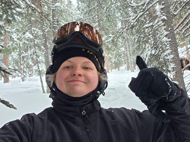 Finn in goggles giving a thumbs up among snowy trees